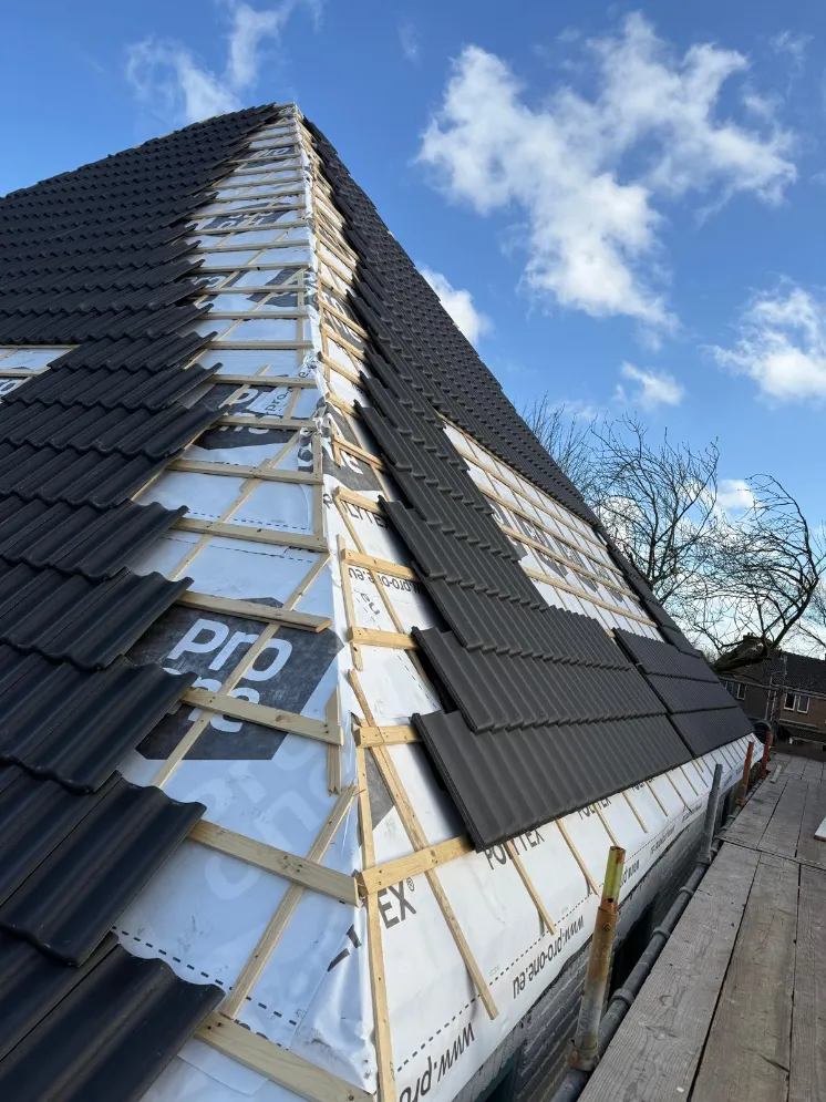 Antracietkleurige dakpannen worden op de nieuwe panlatten gelegd